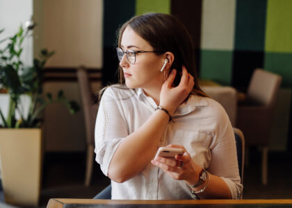 “Close-up of AirPods in ears with iPhone showing paused music, illustrating why do my AirPods keep pausing issue.”